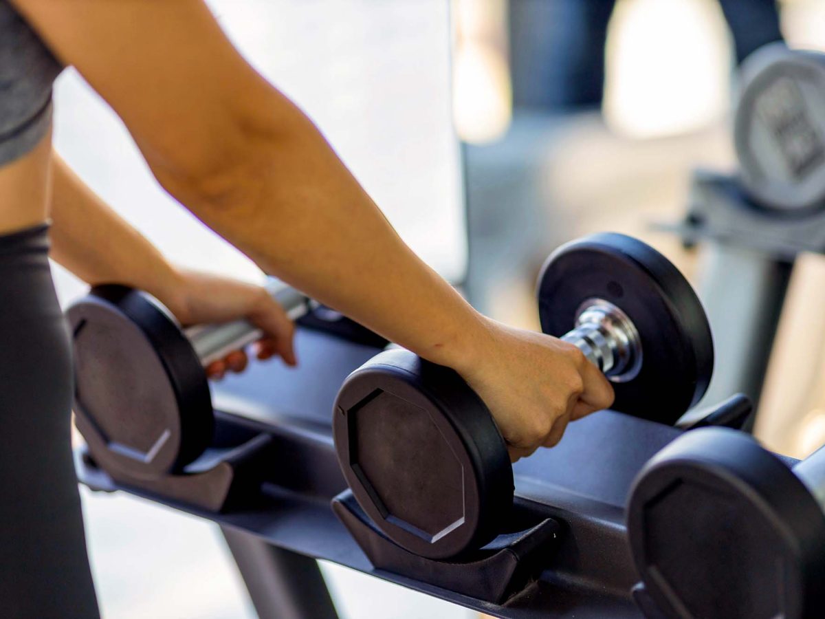 Close up of woman hand choosing dumbbell inside the sport gym for muscle body building, weight lifting and exercise